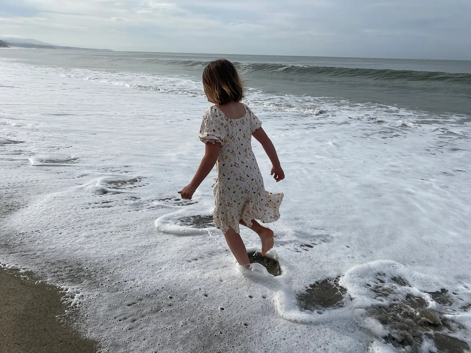 A young girl wearing a dress runs in the surf — Doheny State Beach